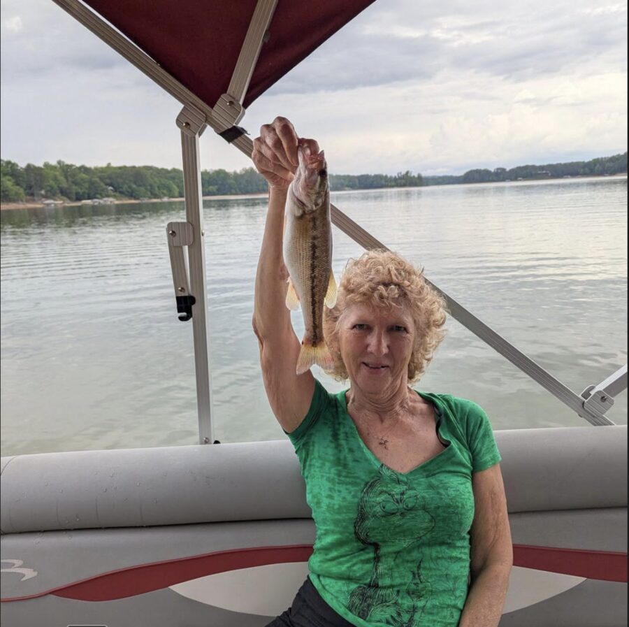 Joan smiling on a pontoon boat, holding up a freshly caught fish