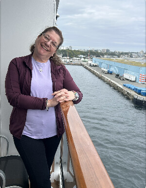 Leslie smiling on the deck of a cruise ship overlooking the harbor